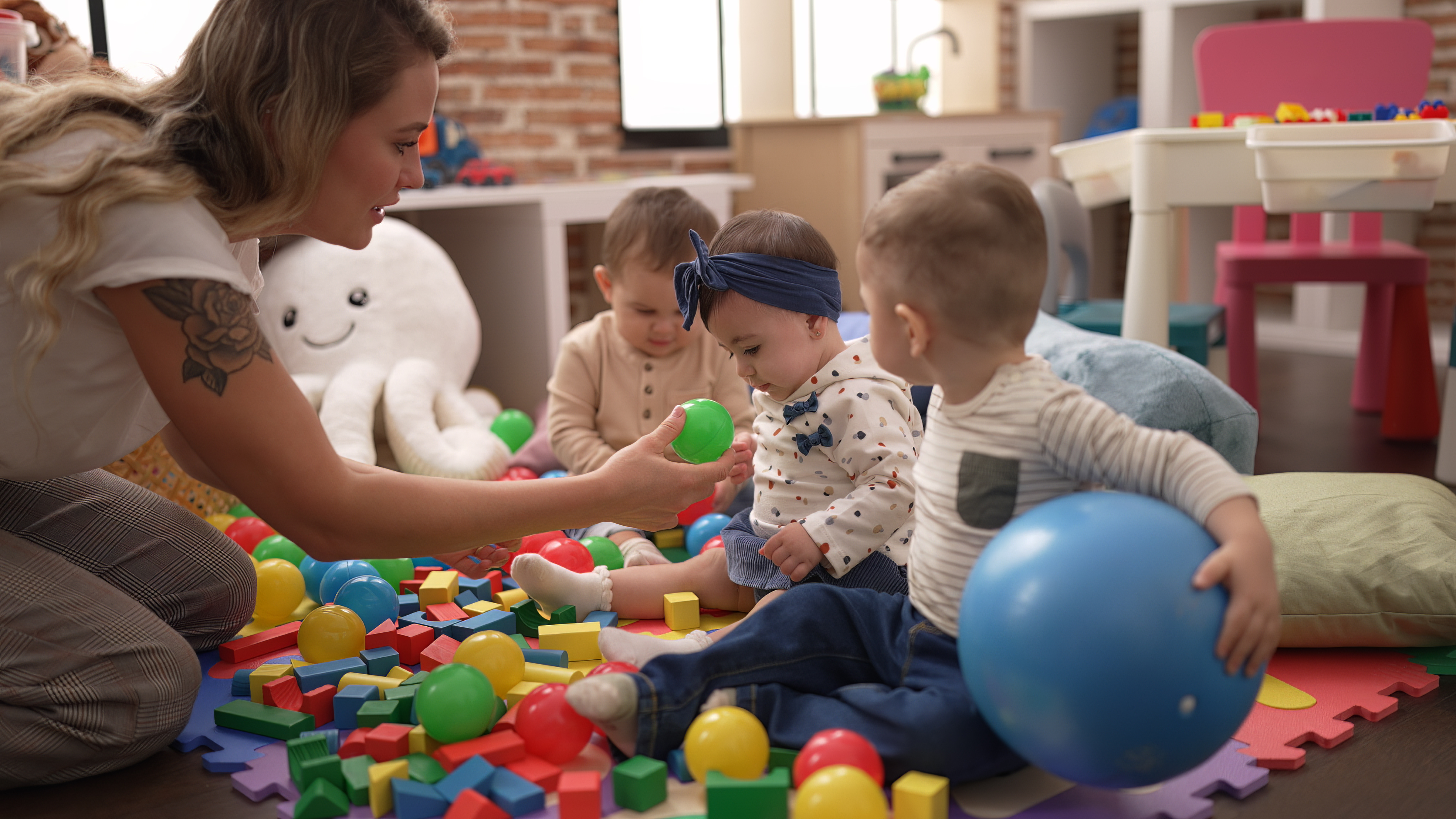 enseignant-et-eleves-d-age-prescolaire-jouant-avec-des-balles-assis-sur-le-sol-a-la-maternelle.jpg