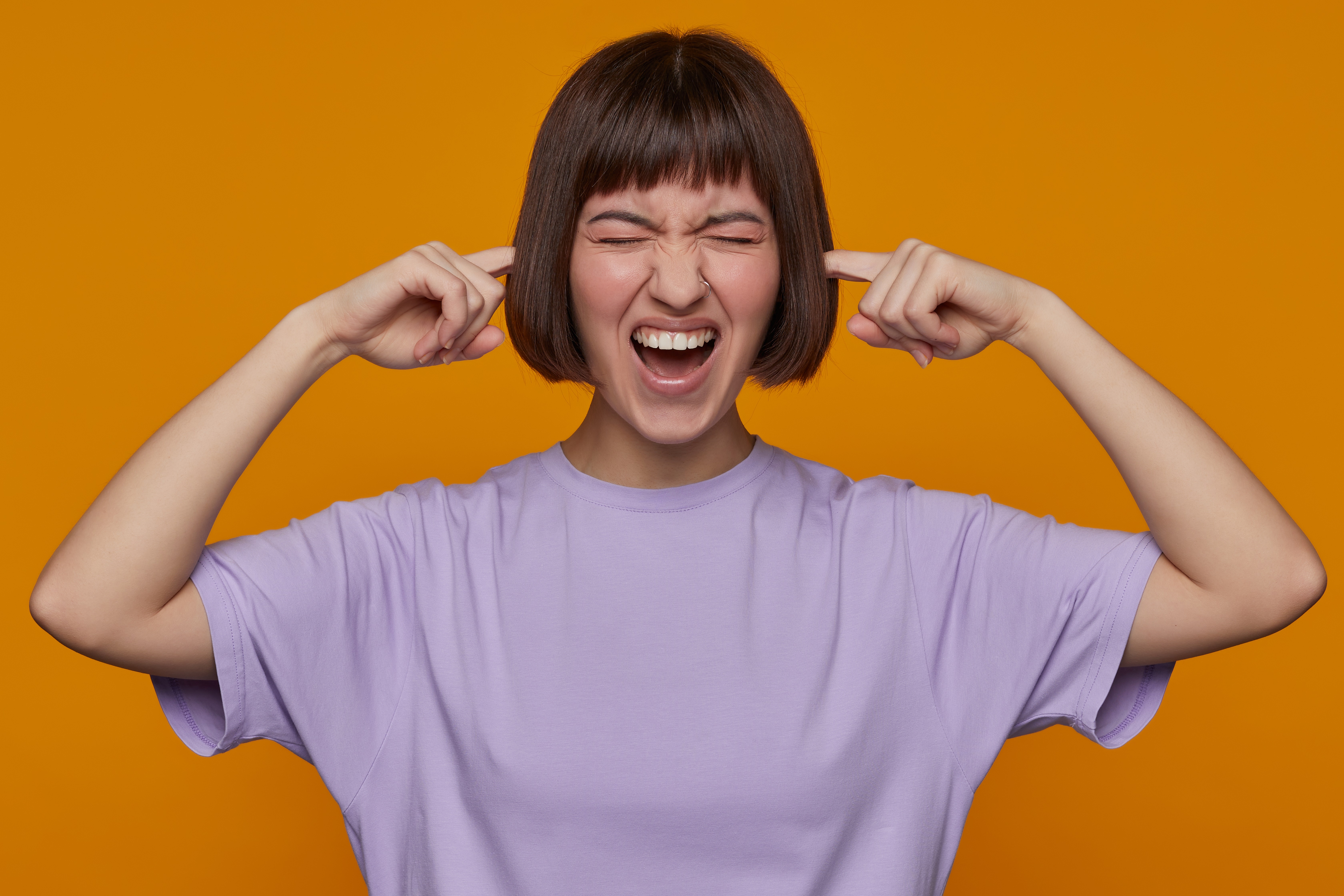 indoor-portrait-of-young-female-posing-over-orange-background-plug-her-ears-with-fingers-stressed-and-depressed.jpg